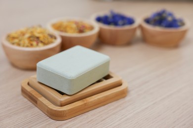 Photo of Soap bar and bowls of dry flowers on light wooden table, space for text. Spa therapy