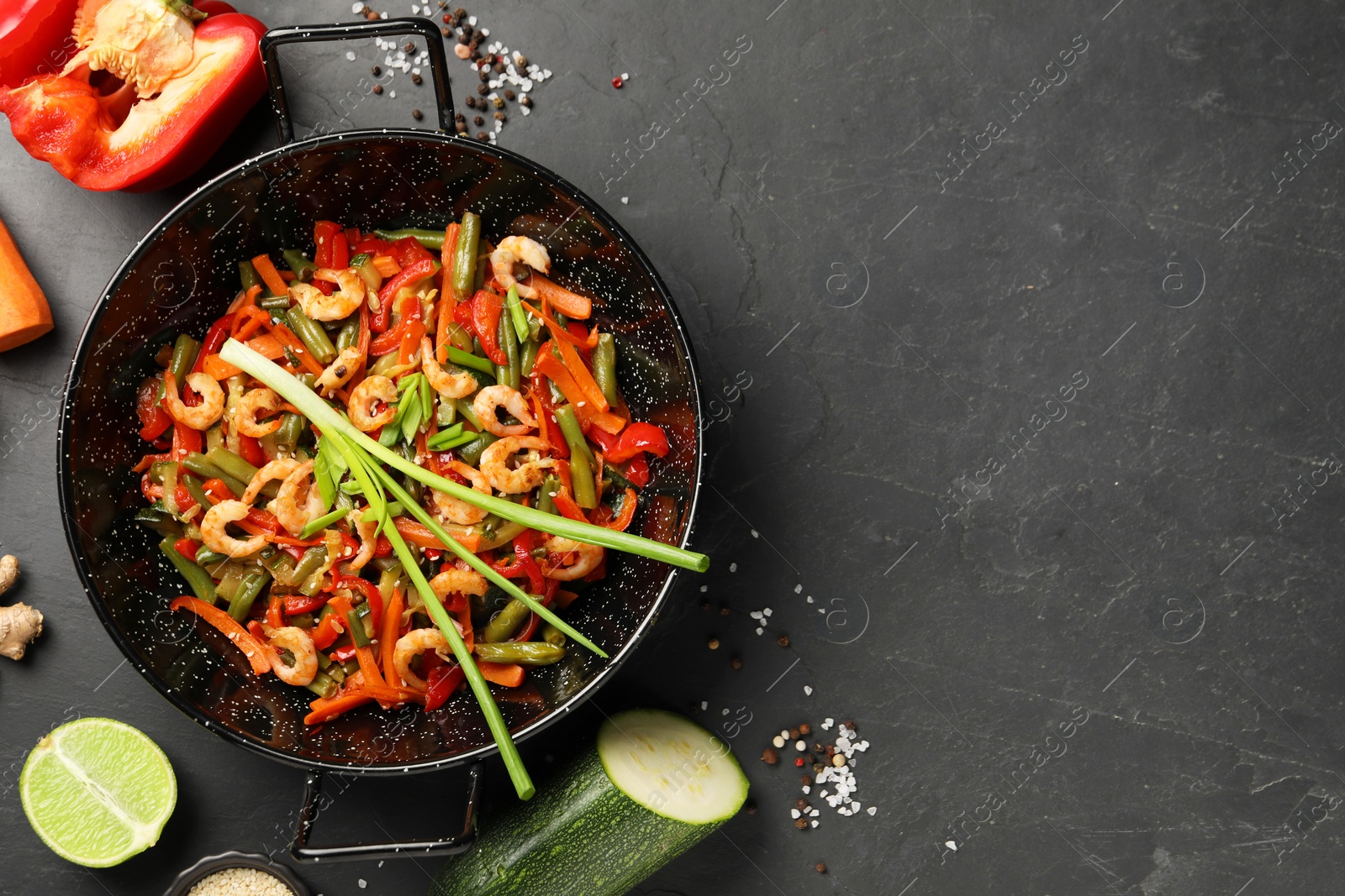 Photo of Shrimp stir fry with vegetables in wok and ingredients on black table, flat lay. Space for text