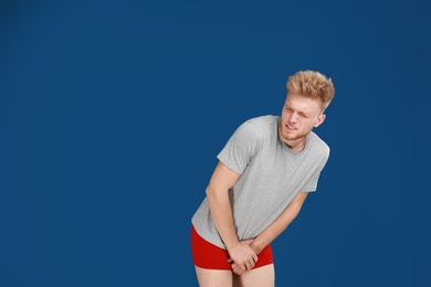 Young man suffering from pain on blue background, space for text. Urology problems