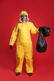 Photo of Woman in chemical protective suit holding trash bag on red background. Virus research