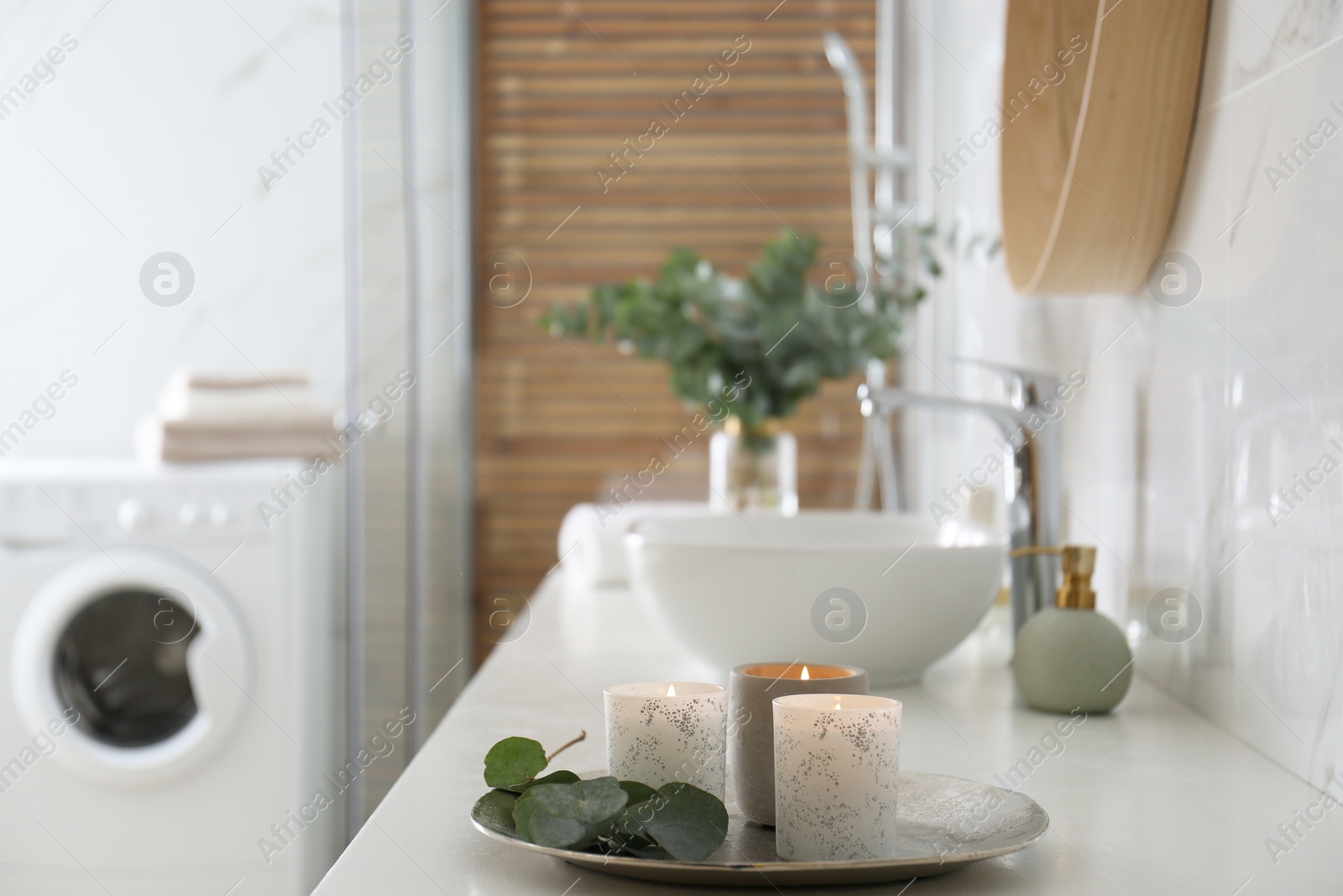 Photo of Tray with eucalyptus leaves and burning candles on countertop in bathroom