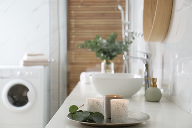 Photo of Tray with eucalyptus leaves and burning candles on countertop in bathroom