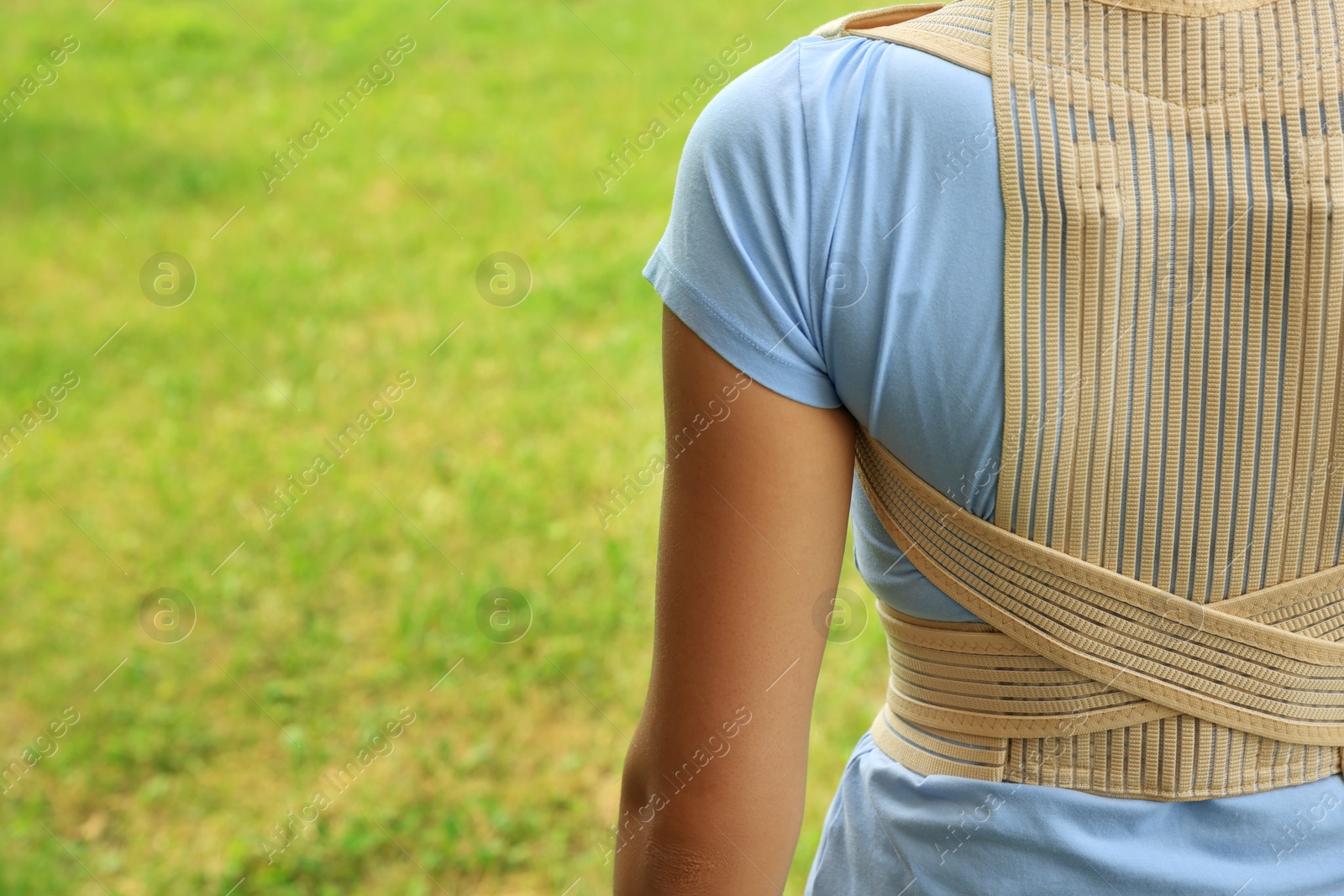 Photo of Closeup of woman with orthopedic corset on green grass outdoors, back view. Space for text