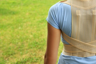 Photo of Closeup of woman with orthopedic corset on green grass outdoors, back view. Space for text