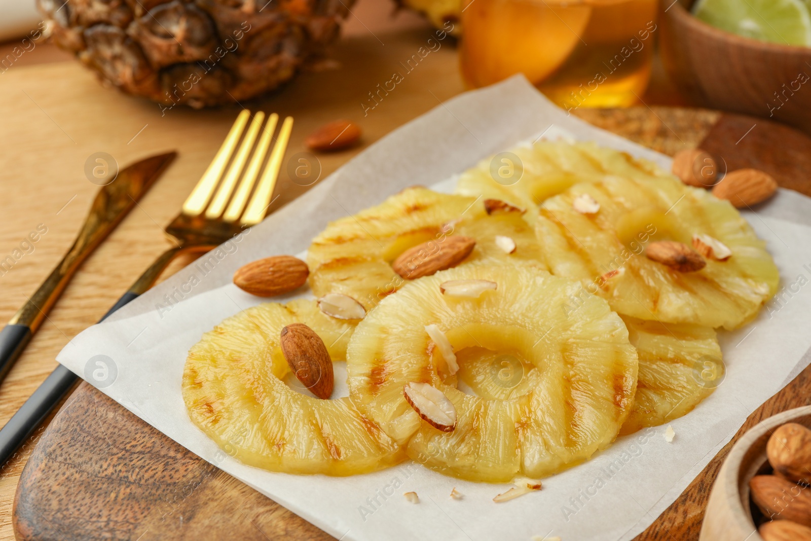 Photo of Tasty grilled pineapple slices and almonds served on wooden table, closeup