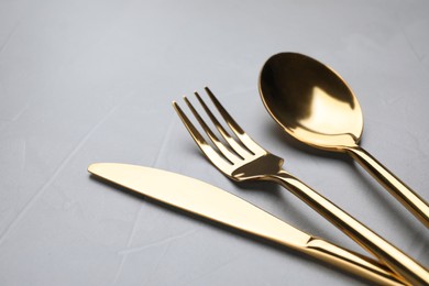 Photo of Set of golden cutlery on grey table, closeup