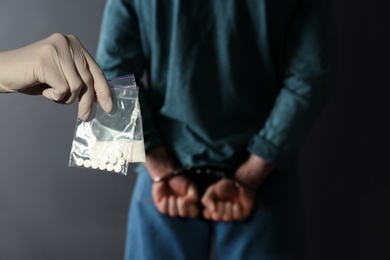 Photo of Police worker holding drugs in plastic bags near arrested dealer on color background