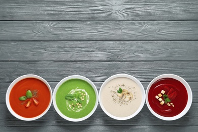 Photo of Various soups in bowls and space for text on wooden background, top view. Healthy food