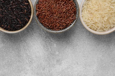 Bowls with different sorts of rice on grey table, flat lay. Space for text