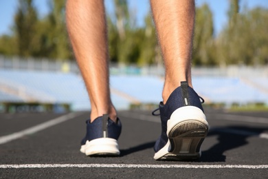 Photo of Sporty man running at stadium on sunny morning, focus on legs