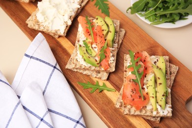 Photo of Fresh crunchy crispbreads with cream cheese, salmon, avocado and arugula on beige table