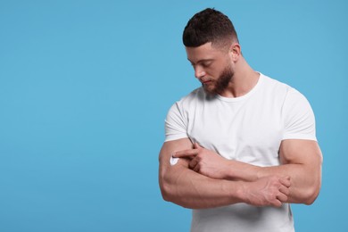 Photo of Handsome man applying body cream onto his arm on light blue background, space for text