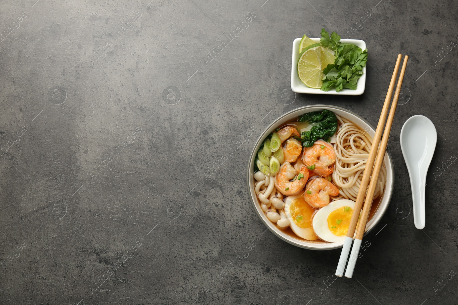 Photo of Delicious ramen with shrimps in bowl served on grey table, flat lay with space for text. Noodle soup