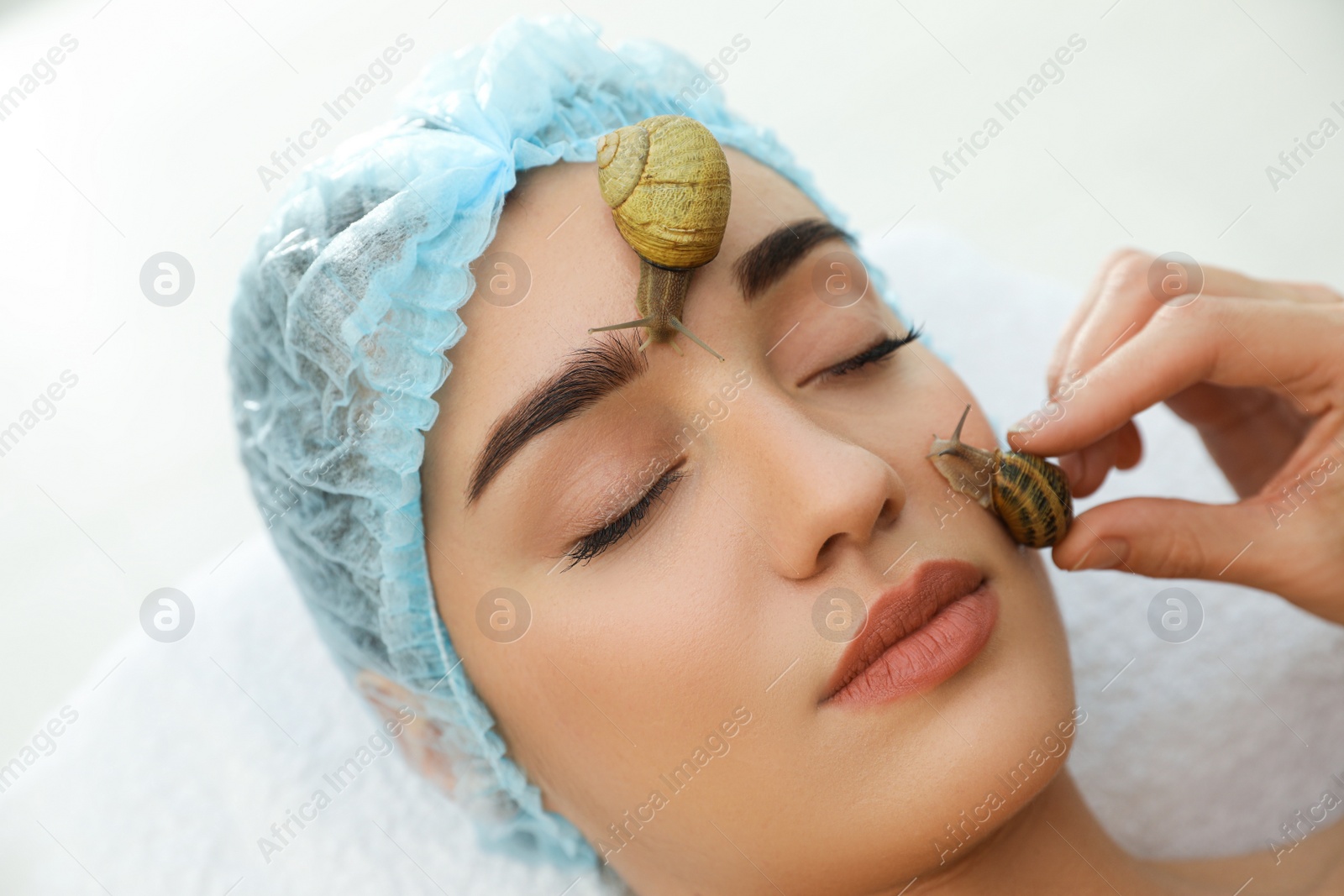 Photo of Young woman receiving snail facial massage in spa salon, closeup