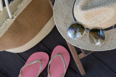 Photo of Stylish hat with sunglasses, bag and flip flops on wooden floor, above view. Beach accessories