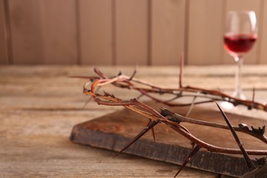Photo of Crown of thorns and glass with wine on wooden table, selective focus. Space for text