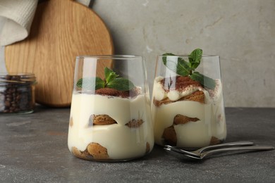 Photo of Delicious tiramisu with mint in glasses on grey table