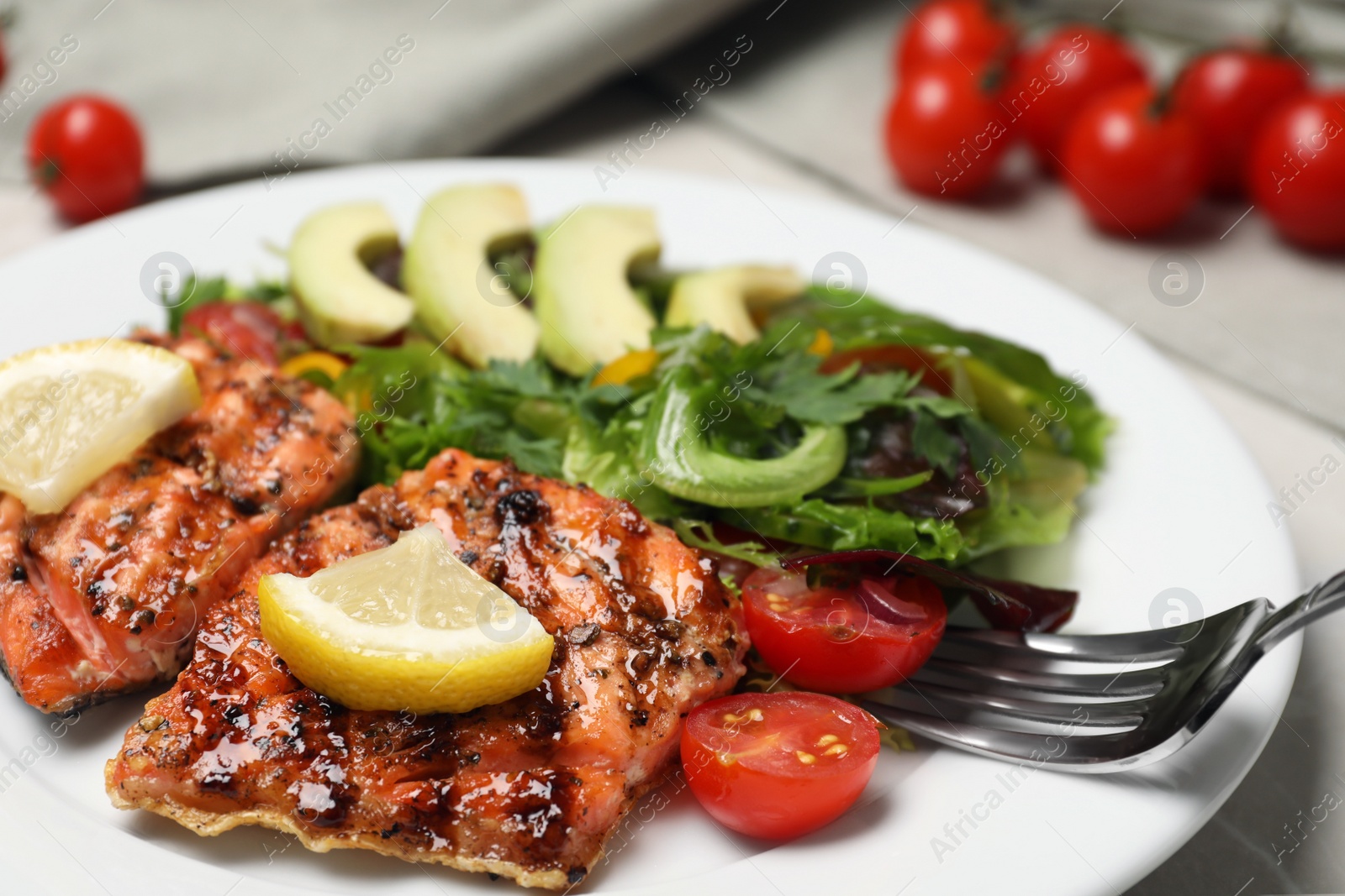 Photo of Tasty grilled salmon with lemon and tomatoes on light grey table, closeup