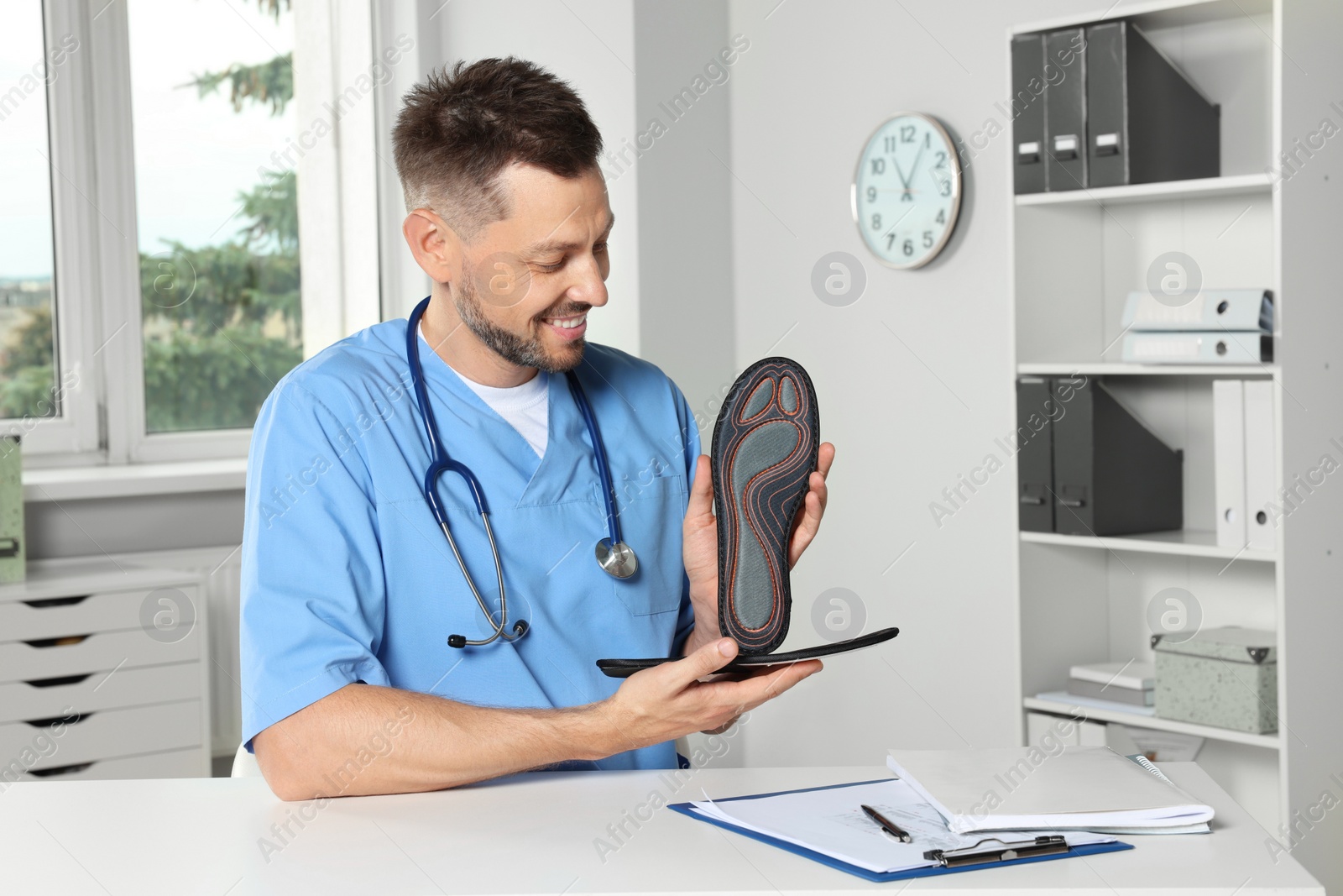 Photo of Handsome male orthopedist showing insoles in hospital