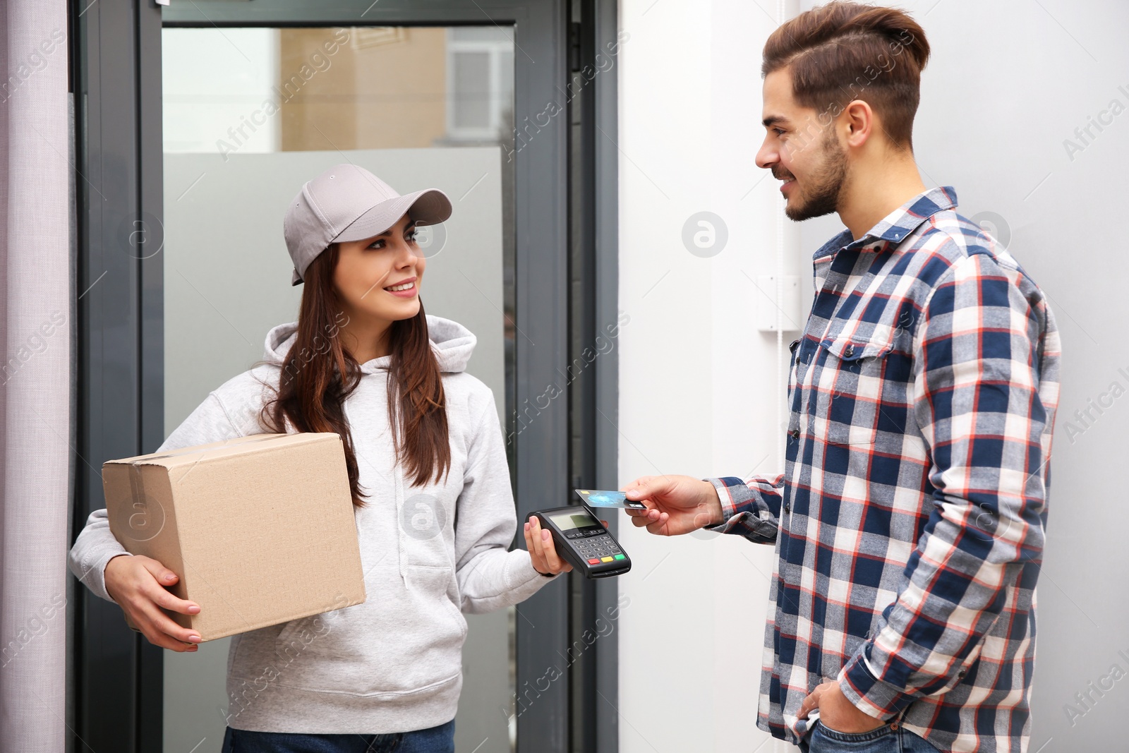 Photo of Young man with credit card using bank terminal for delivery payment at doorway