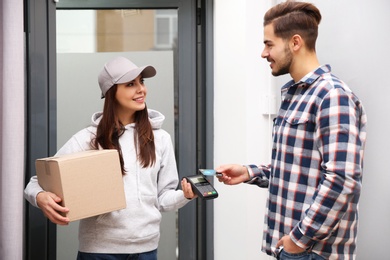 Photo of Young man with credit card using bank terminal for delivery payment at doorway