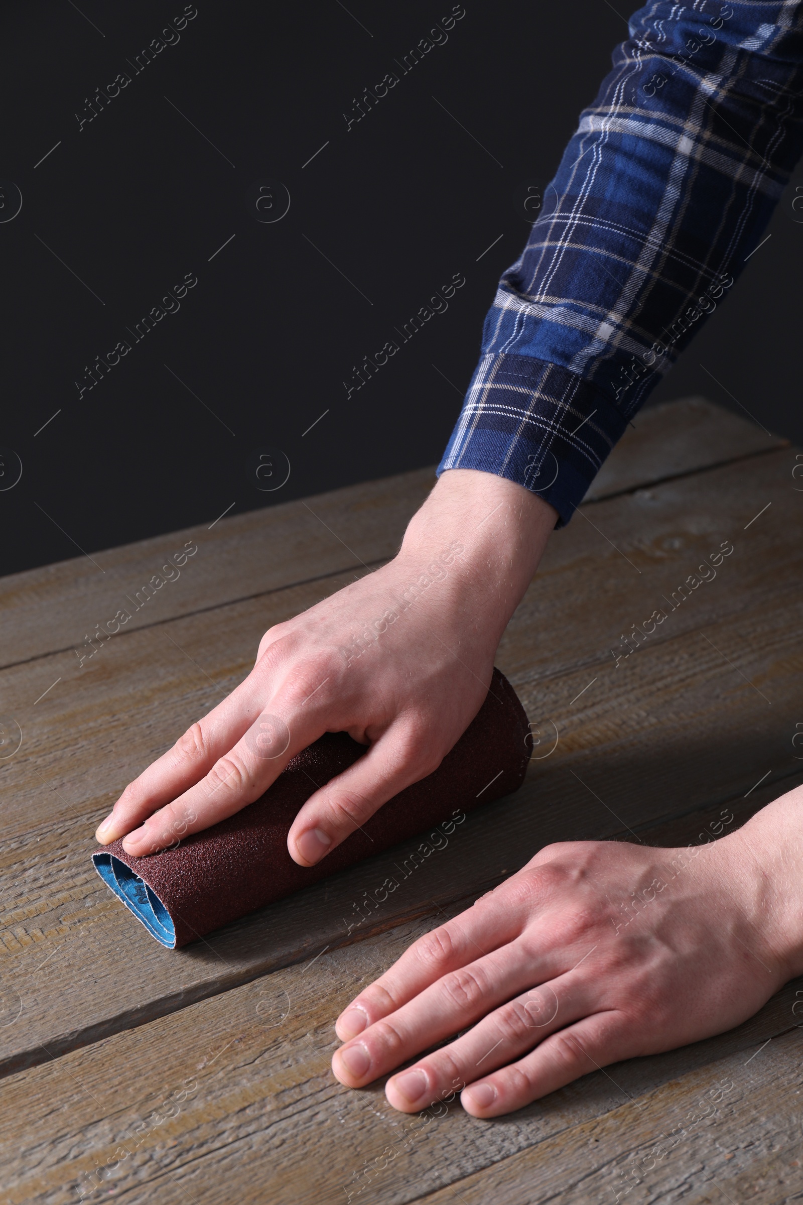 Photo of Man polishing wooden table with rolled sheet of sandpaper, closeup