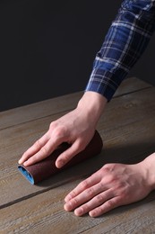 Photo of Man polishing wooden table with rolled sheet of sandpaper, closeup