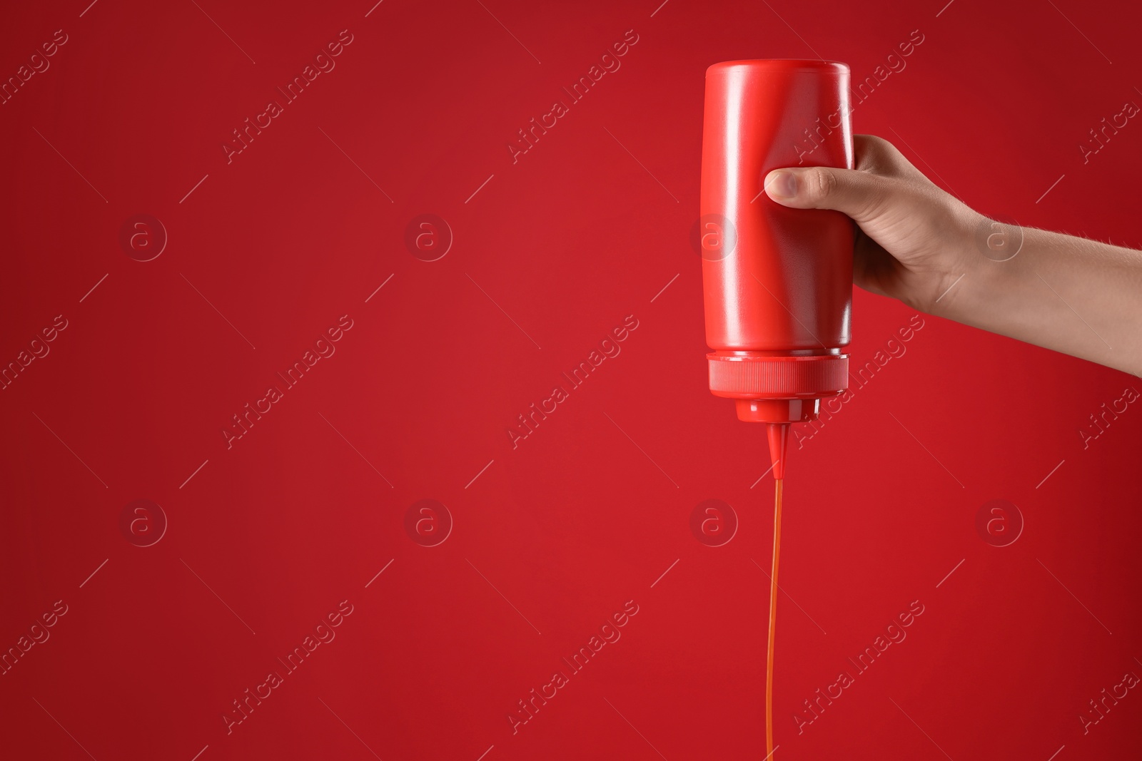 Photo of Woman pouring tasty ketchup from bottle on red background, closeup. Space for text