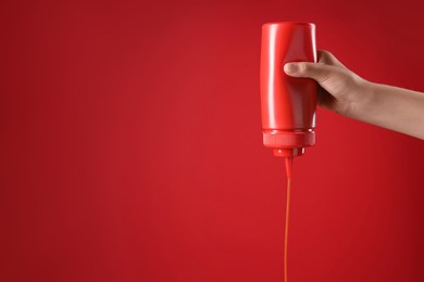 Photo of Woman pouring tasty ketchup from bottle on red background, closeup. Space for text