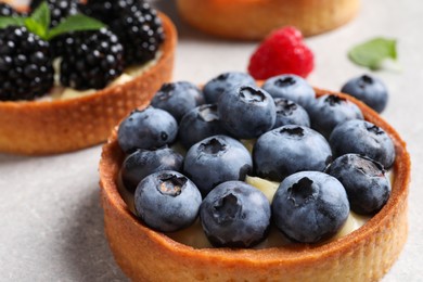 Photo of Tartlets with different fresh berries on light table, closeup. Delicious dessert