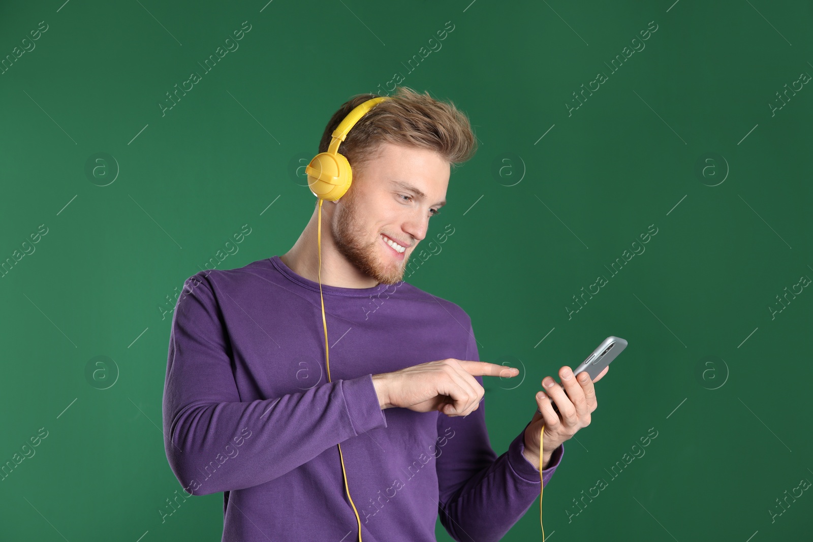 Photo of Handsome young man listening to music with headphones on color background