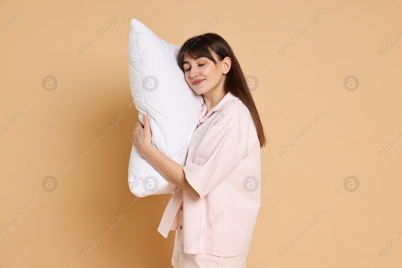 Photo of Woman wearing pyjama and holding pillow on beige background