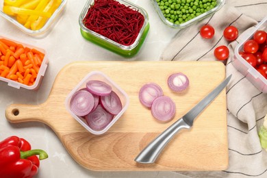 Photo of Wooden board with cut onion, knife and containers with fresh products on light gray table, flat lay. Food storage