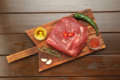 Fresh raw beef cut, spices and oil on wooden table, top view