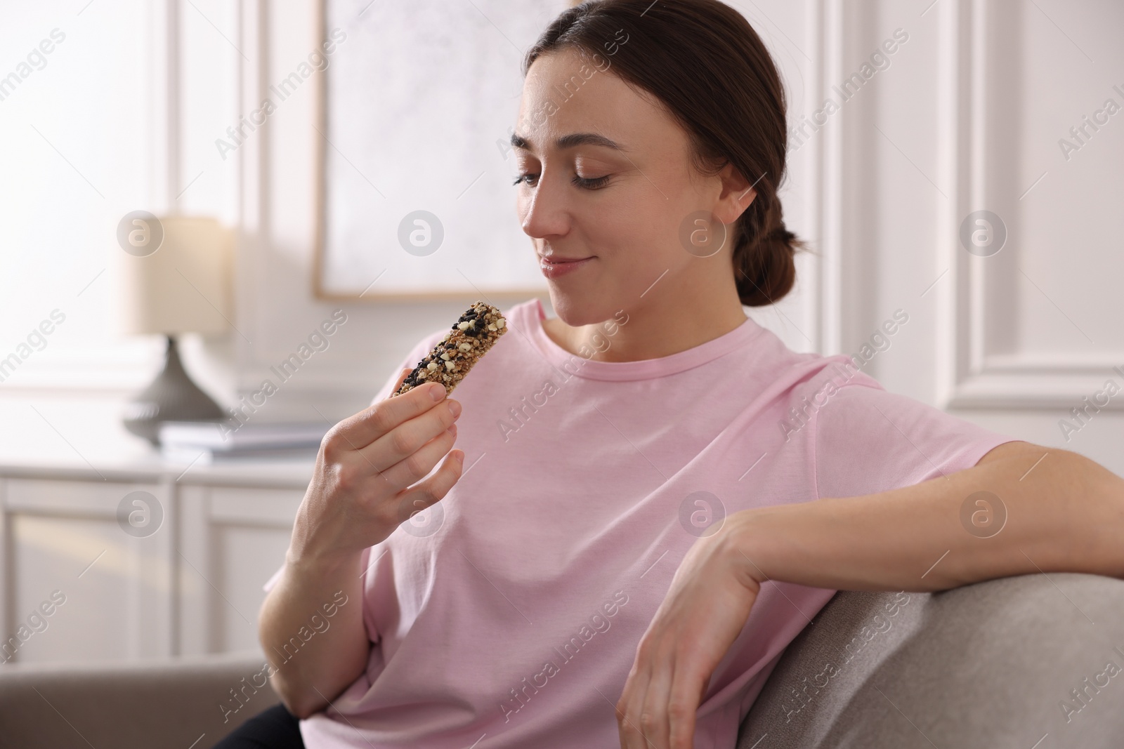 Photo of Woman eating tasty granola bar at home