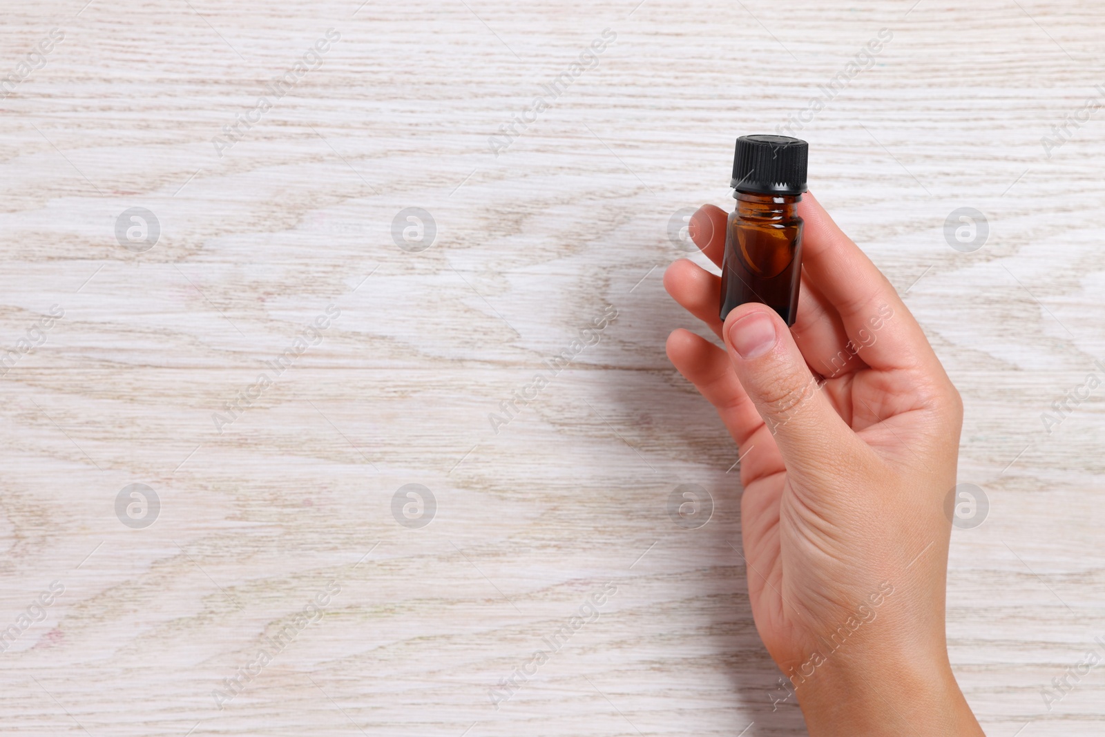 Photo of Woman with bottle of essential oil on wooden background, closeup. Space for text