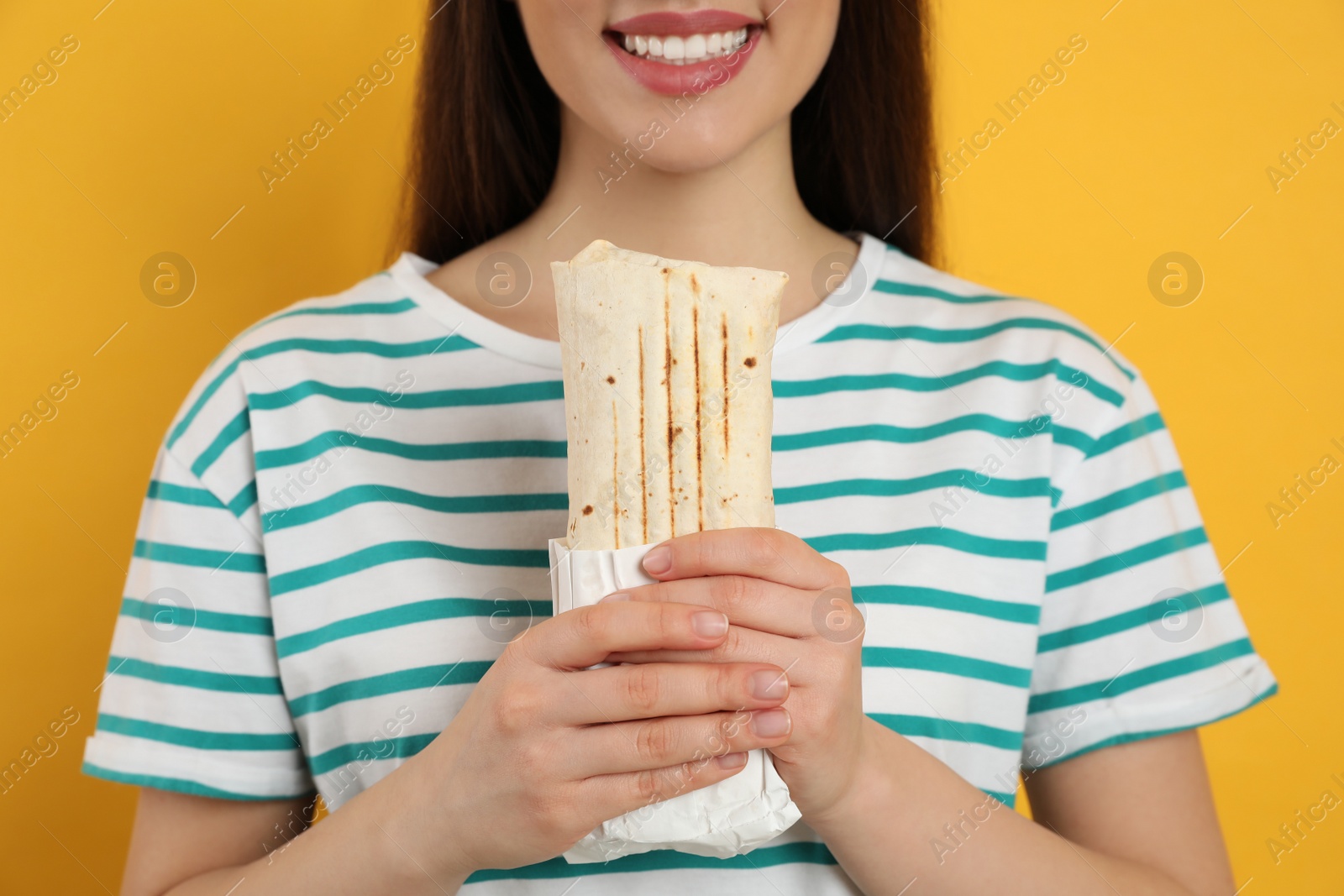 Photo of Happy young woman holding tasty shawarma on yellow background, closeup
