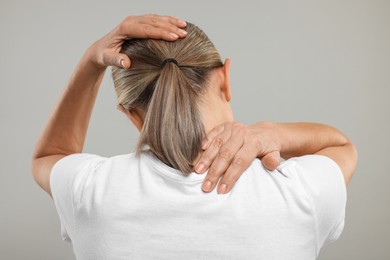 Mature woman suffering from pain in her neck on grey background, back view