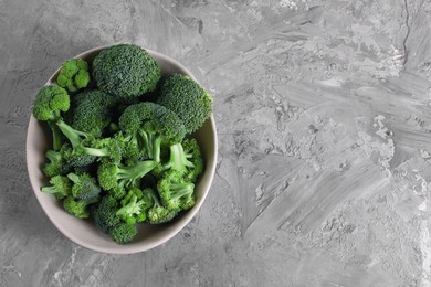 Photo of Bowl of fresh raw broccoli on grey textured table, top view. Space for text