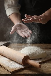 Photo of Man sprinkling flour over dough at wooden table, closeup