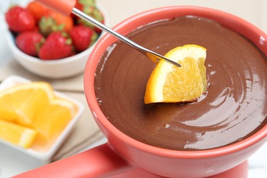 Dipping fresh orange into fondue pot with melted chocolate at table, closeup