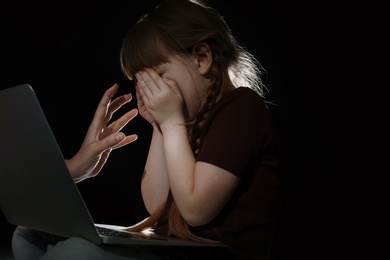 Stranger reaching frightened little child with laptop on dark background. Cyber danger