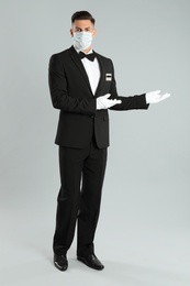 Photo of Waiter wearing medical face mask on light grey background