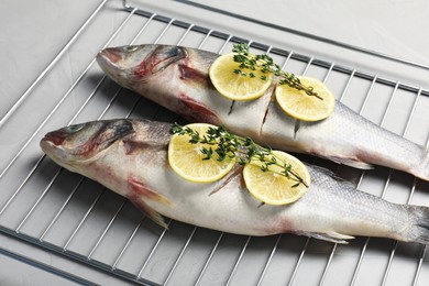 Photo of Oven rack with raw sea bass fish, lemon and thyme on light grey table, closeup