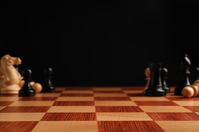 Many chess pieces on wooden checkerboard against black background, selective focus. Space for text