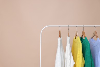 Photo of Rack with different warm sweaters on beige background. Space for text