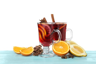 Photo of Glass cups of mulled wine, fresh orange, cinnamon sticks and lemon on table against white background