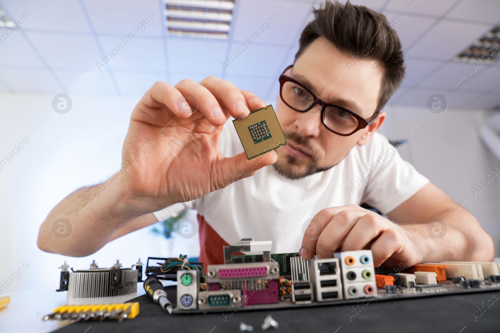 Photo of Male technician repairing motherboard at table indoors