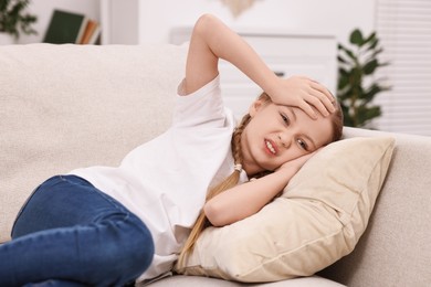 Photo of Little girl suffering from headache on sofa indoors