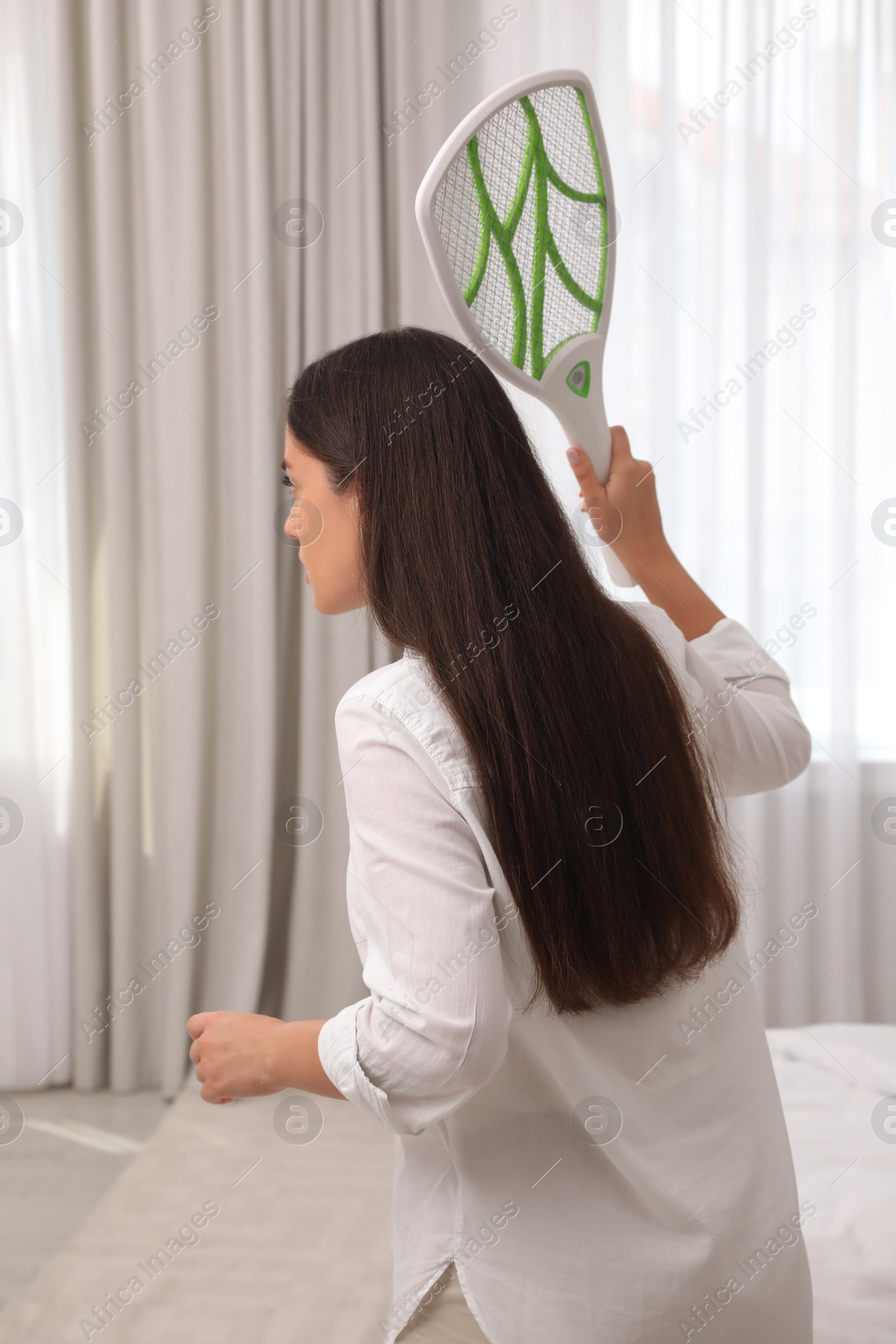 Photo of Young woman with electric fly swatter indoors, back view. Insect killer